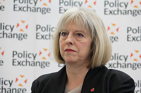 A photo of PM Theresa May, against a background showing the Policy Exchange logo